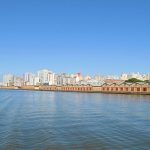 Vista panorâmica da orla de Porto Alegre às margens do Guaíba, com o horizonte da cidade ao fundo.