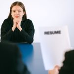 Candidata participa de uma entrevista de emprego diante de dois recrutadores, com o currículo sobre a mesa.
