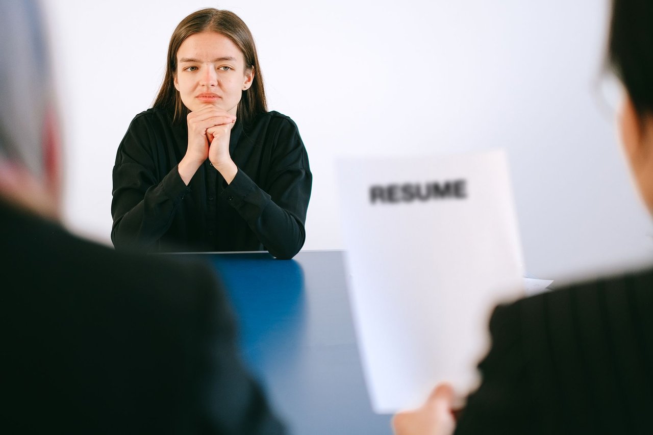 Candidata participa de uma entrevista de emprego diante de dois recrutadores, com o currículo sobre a mesa.
